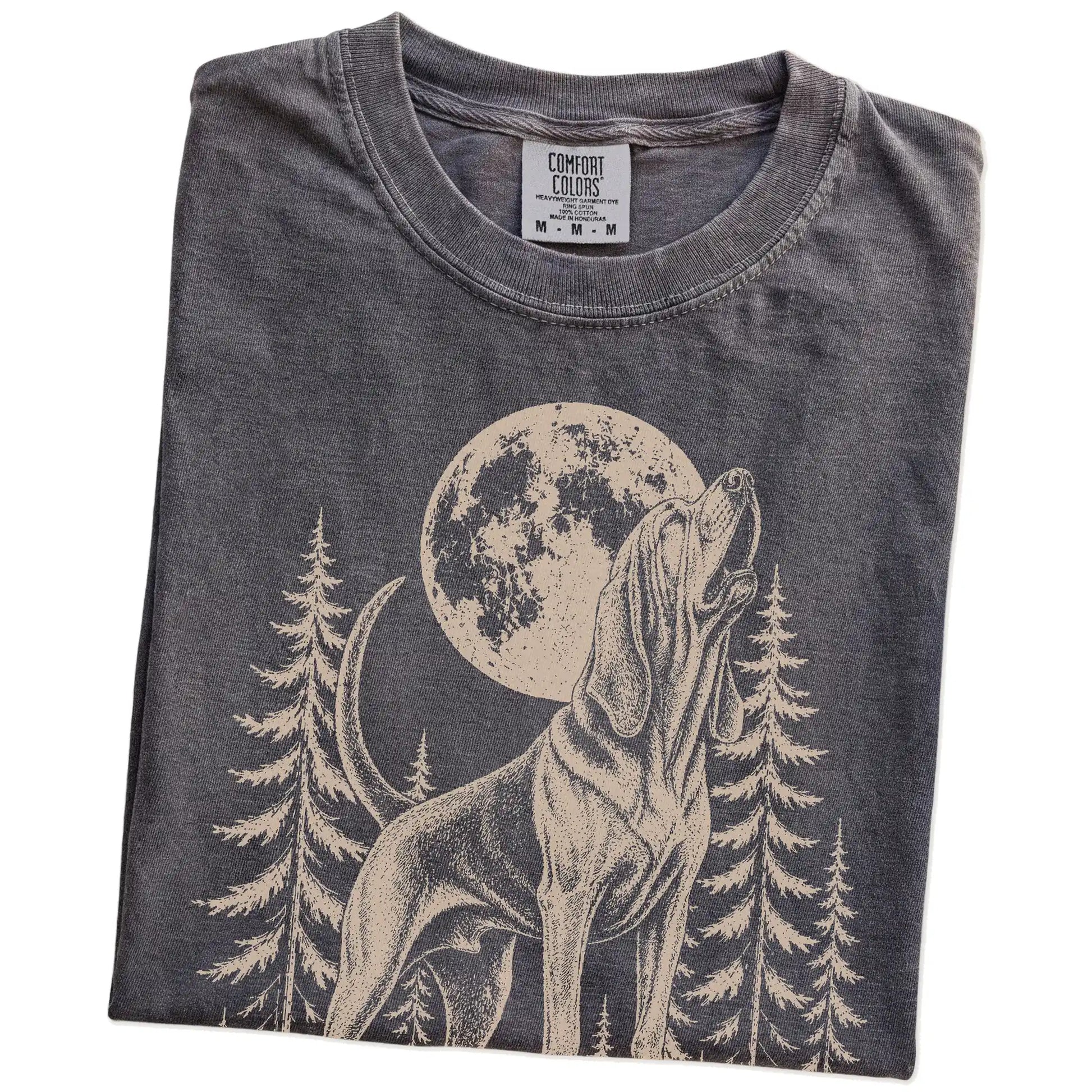Folded Pepper Comfort Colors® T-shirt showing a Bloodhound howling beneath the moon and pine trees