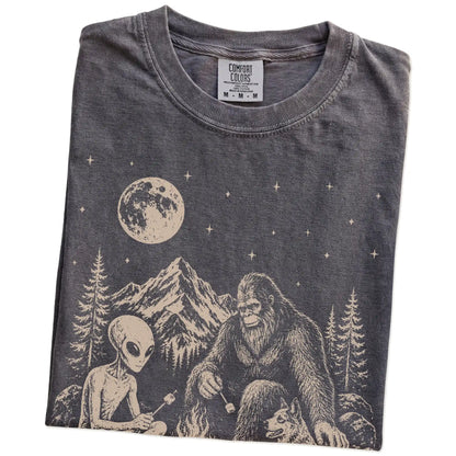 Folded Pepper Comfort Colors® T-shirt showing Blue Heeler camping with Bigfoot and an alien