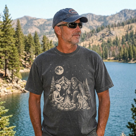 Model wearing a Pepper Comfort Colors® T-shirt showing Blue Heeler camping with Bigfoot and an alien