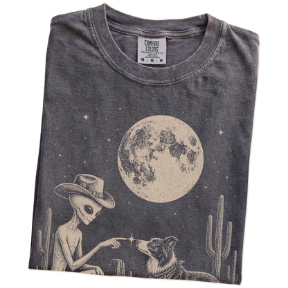 Folded Pepper Comfort Colors® T-shirt showing cowboy alien fist-bumping a border collie beneath the moon