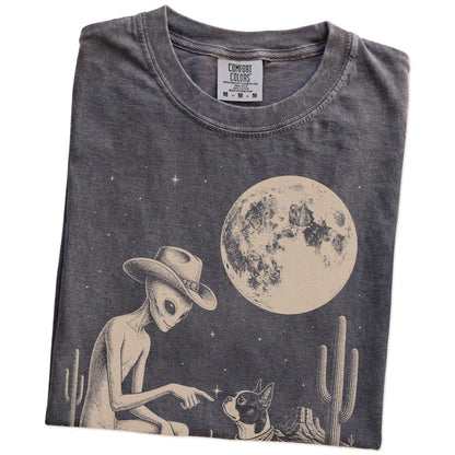 Folded Pepper Comfort Colors® T-shirt showing cowboy alien fist-bumping a boston terrier beneath the moon