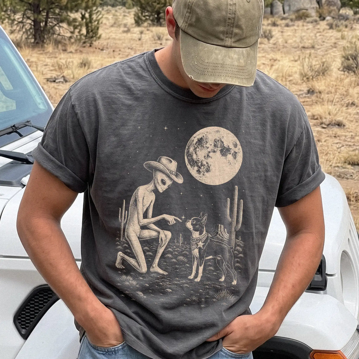 Model wearing a Pepper Comfort Colors® T-shirt with cowboy alien fist-bumping a boston terrier beneath the moon