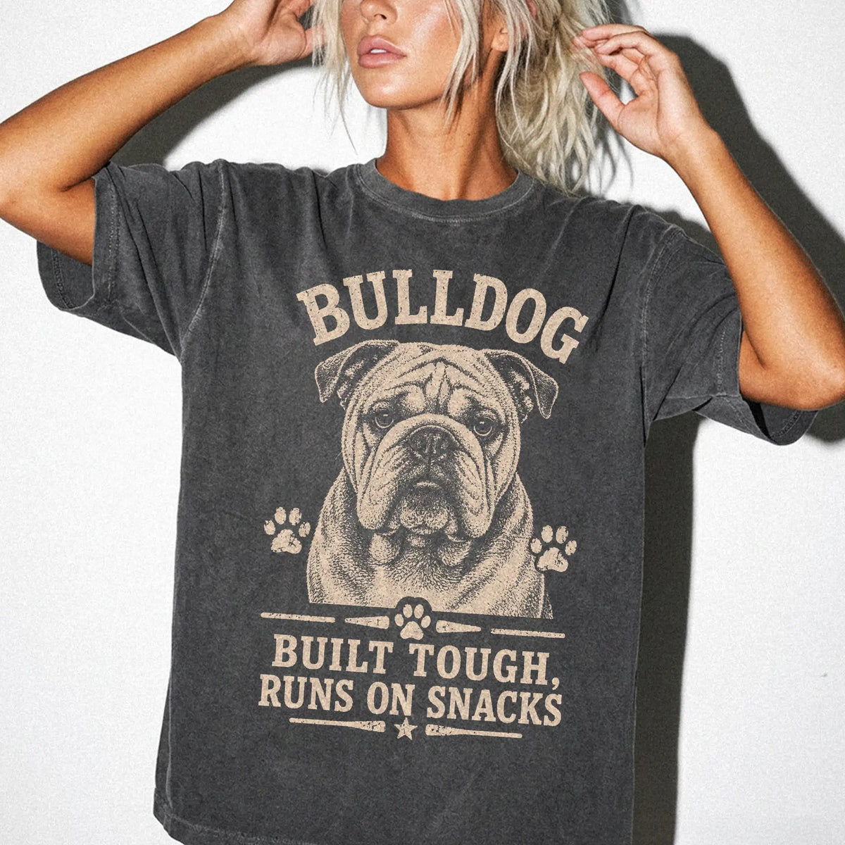 Model wearing a Pepper Comfort Colors® T-shirt featuring Bulldog design with “Built Tough, Runs On Snacks” lettering