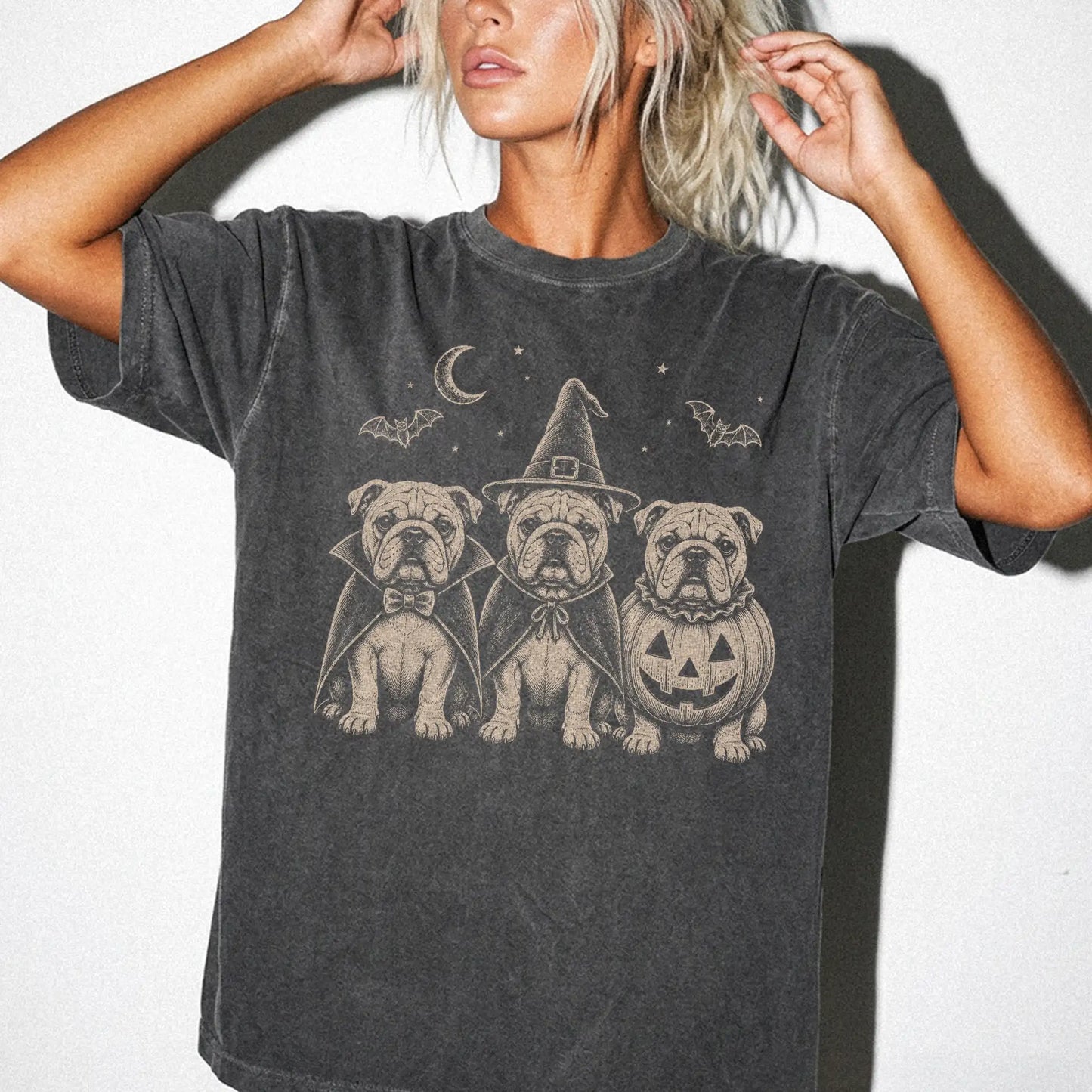Model wearing a Pepper Comfort Colors® T-shirt showing three Bulldog dogs dressed for Halloween beneath bats and a crescent m