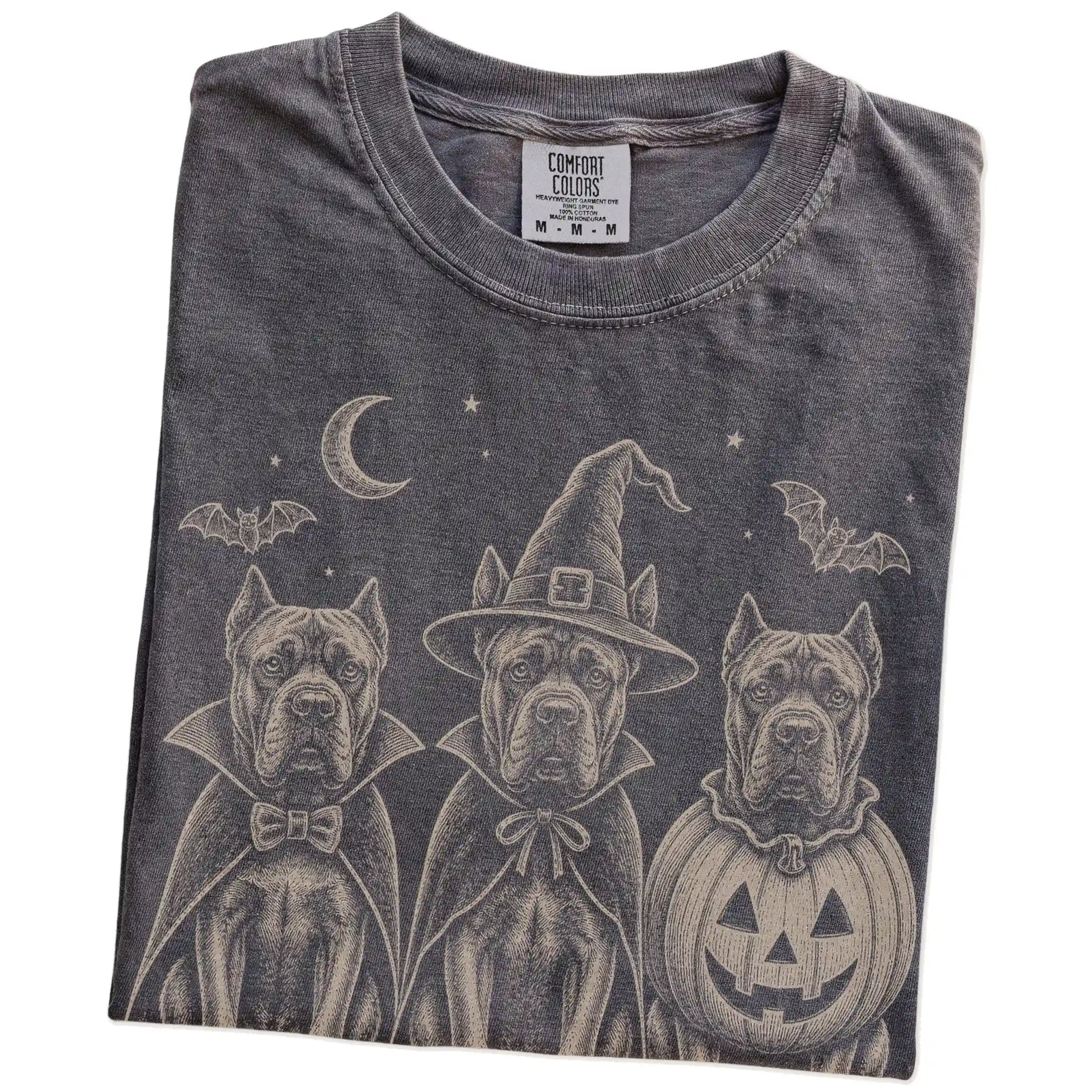 Folded Pepper Comfort Colors® T-shirt showing three Cane Corso dogs dressed for Halloween beneath bats and a crescent moon