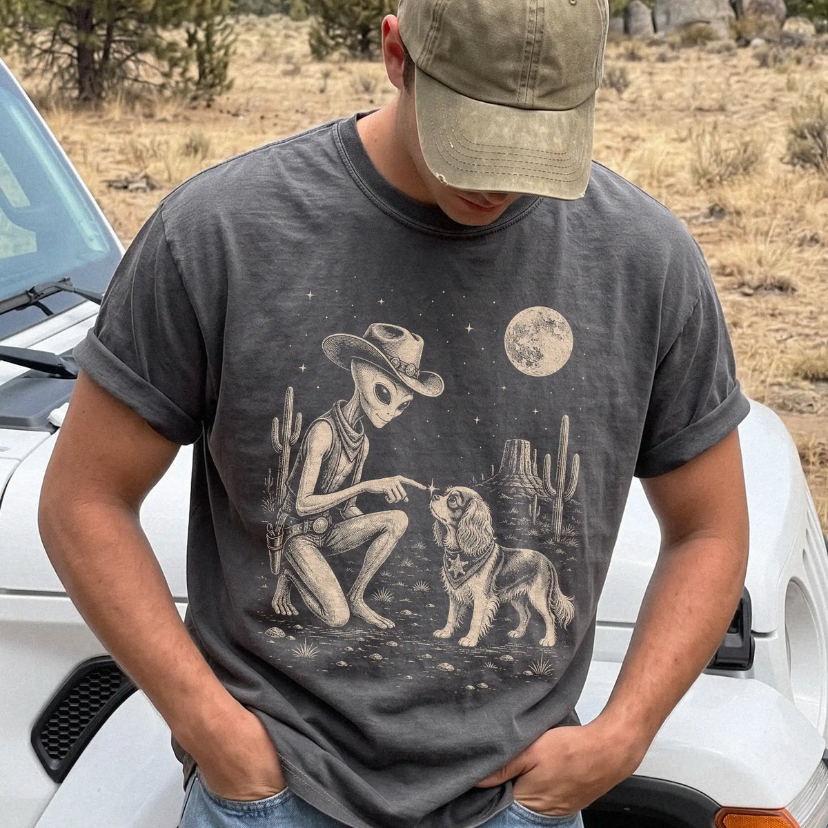 Model wearing a Pepper Comfort Colors® T-shirt with cowboy alien fist-bumping a cavalier king charles spaniel beneath the moon