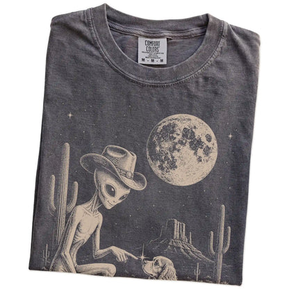 Folded Pepper Comfort Colors® T-shirt showing cowboy alien fist-bumping a cocker spaniel beneath the moon