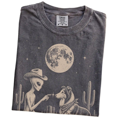 Folded Pepper Comfort Colors® T-shirt showing cowboy alien fist-bumping a collie beneath the moon