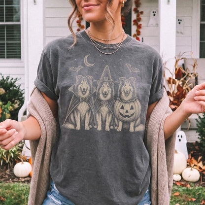 Model wearing a Pepper Comfort Colors® T-shirt showing three Collie dogs dressed for Halloween beneath bats and a crescent mo