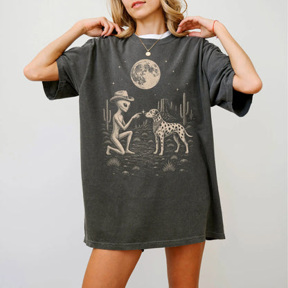 Model wearing a Pepper Comfort Colors® T-shirt with cowboy alien fist-bumping a dalmatian beneath the moon