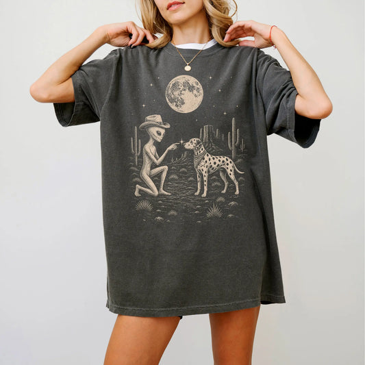 Model wearing a Pepper Comfort Colors® T-shirt with cowboy alien fist-bumping a dalmatian beneath the moon