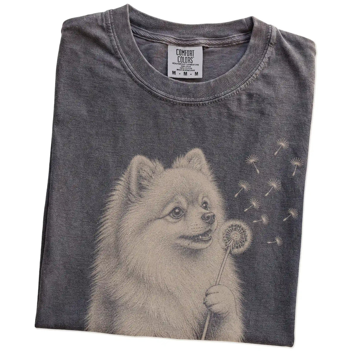 Folded Pepper Comfort Colors® T-shirt showing Pomeranian portrait with drifting dandelion seeds