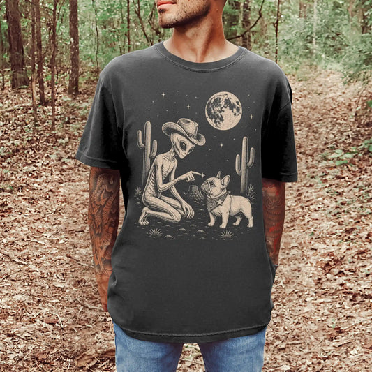 Model wearing a Pepper Comfort Colors® T-shirt with cowboy alien fist-bumping a french bulldog beneath the moon