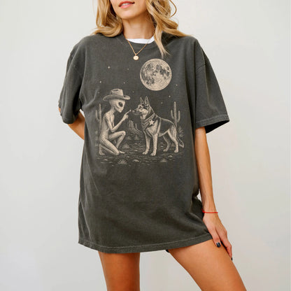 Model wearing a Pepper Comfort Colors® T-shirt with cowboy alien fist-bumping a german shepherd beneath the moon