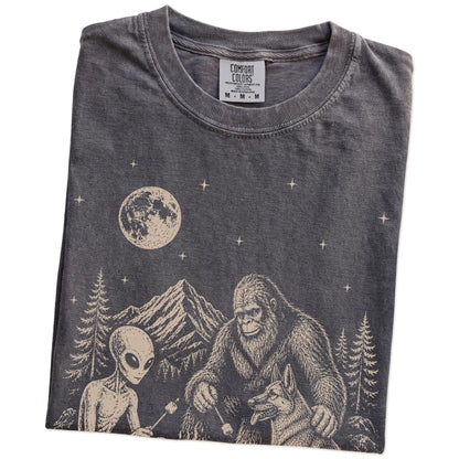 Folded Pepper Comfort Colors® T-shirt showing German Shepherd camping with Bigfoot and an alien