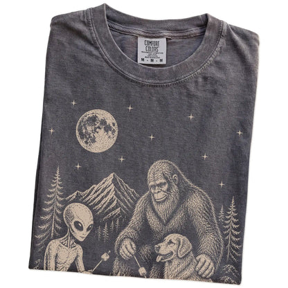 Folded Pepper Comfort Colors® T-shirt showing Golden Retriever camping with Bigfoot and an alien