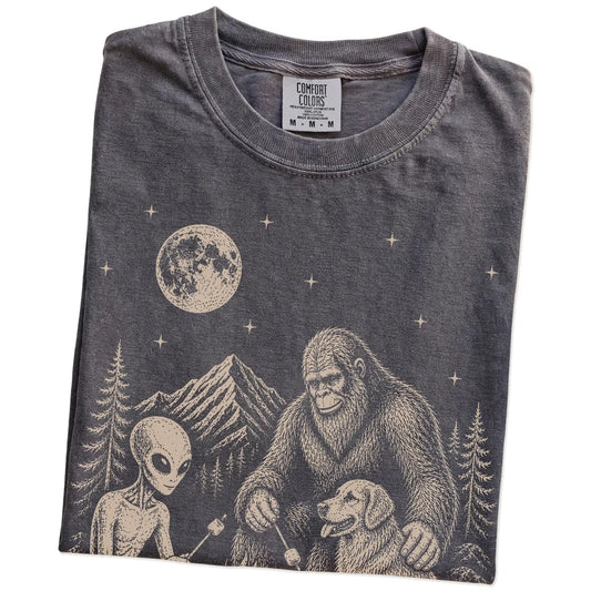 Folded Pepper Comfort Colors® T-shirt showing Golden Retriever camping with Bigfoot and an alien