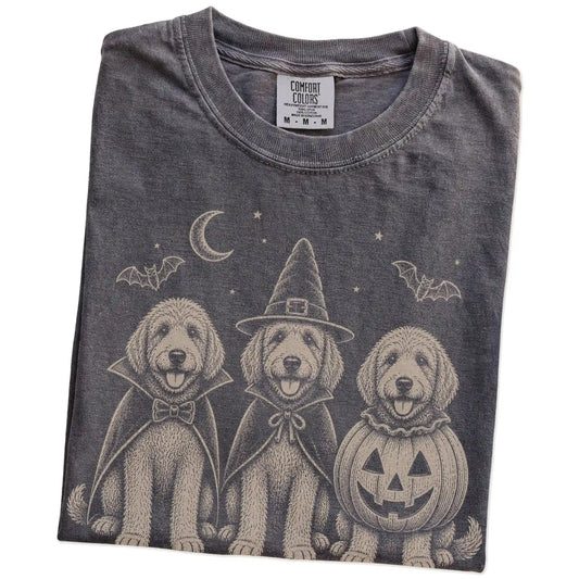 Folded Pepper Comfort Colors® T-shirt showing three Goldendoodle dogs dressed for Halloween beneath bats and a crescent moon