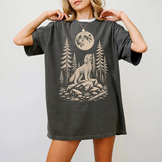 Model wearing a Pepper Comfort Colors® T-shirt with a Goldendoodle howling beneath the moon and pine trees