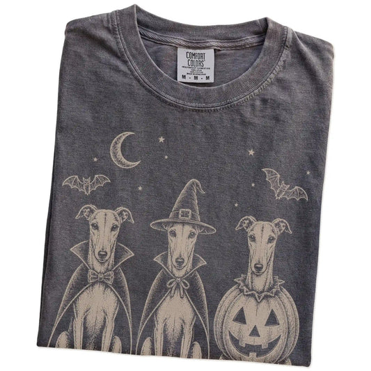 Folded Pepper Comfort Colors® T-shirt showing three Greyhound dogs dressed for Halloween beneath bats and a crescent moon