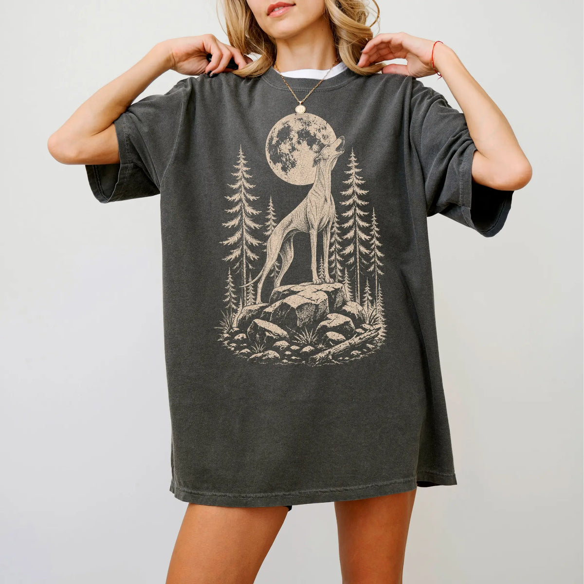 Model wearing a Pepper Comfort Colors® T-shirt with a Greyhound howling beneath the moon and pine trees