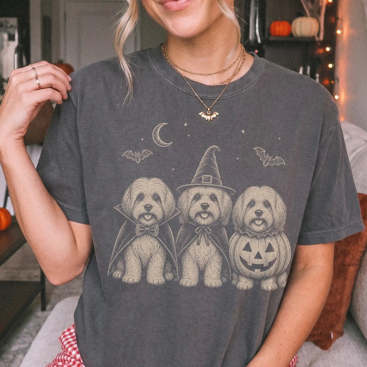 Model wearing a Pepper Comfort Colors® T-shirt showing three Havanese dogs dressed for Halloween beneath bats and a crescent 