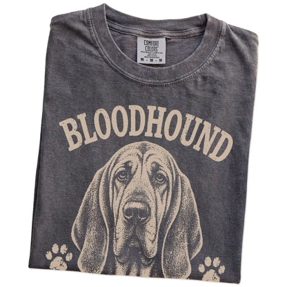 Folded Pepper Comfort Colors® T-shirt showing Bloodhound design with “I Never Forget A Scent Or A Grudge” lettering