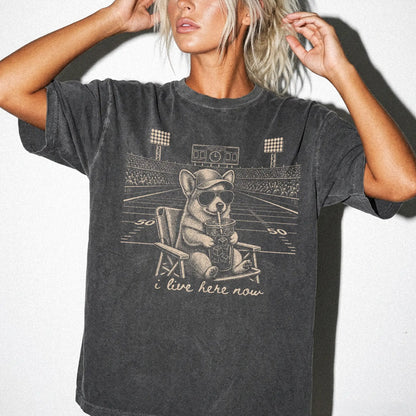 Model wearing a Pepper Comfort Colors® T-shirt featuring Corgi claiming the football field with “I Live Here Now” lettering
