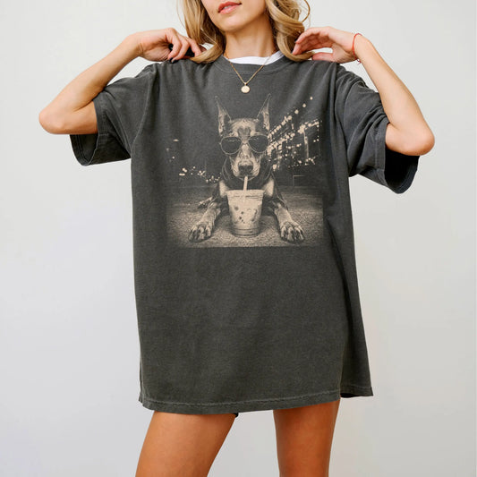 Model wearing a Pepper Comfort Colors® T-shirt featuring Doberman with iced coffee in a retro grunge design