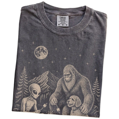 Folded Pepper Comfort Colors® T-shirt showing Labradoodle camping with Bigfoot and an alien