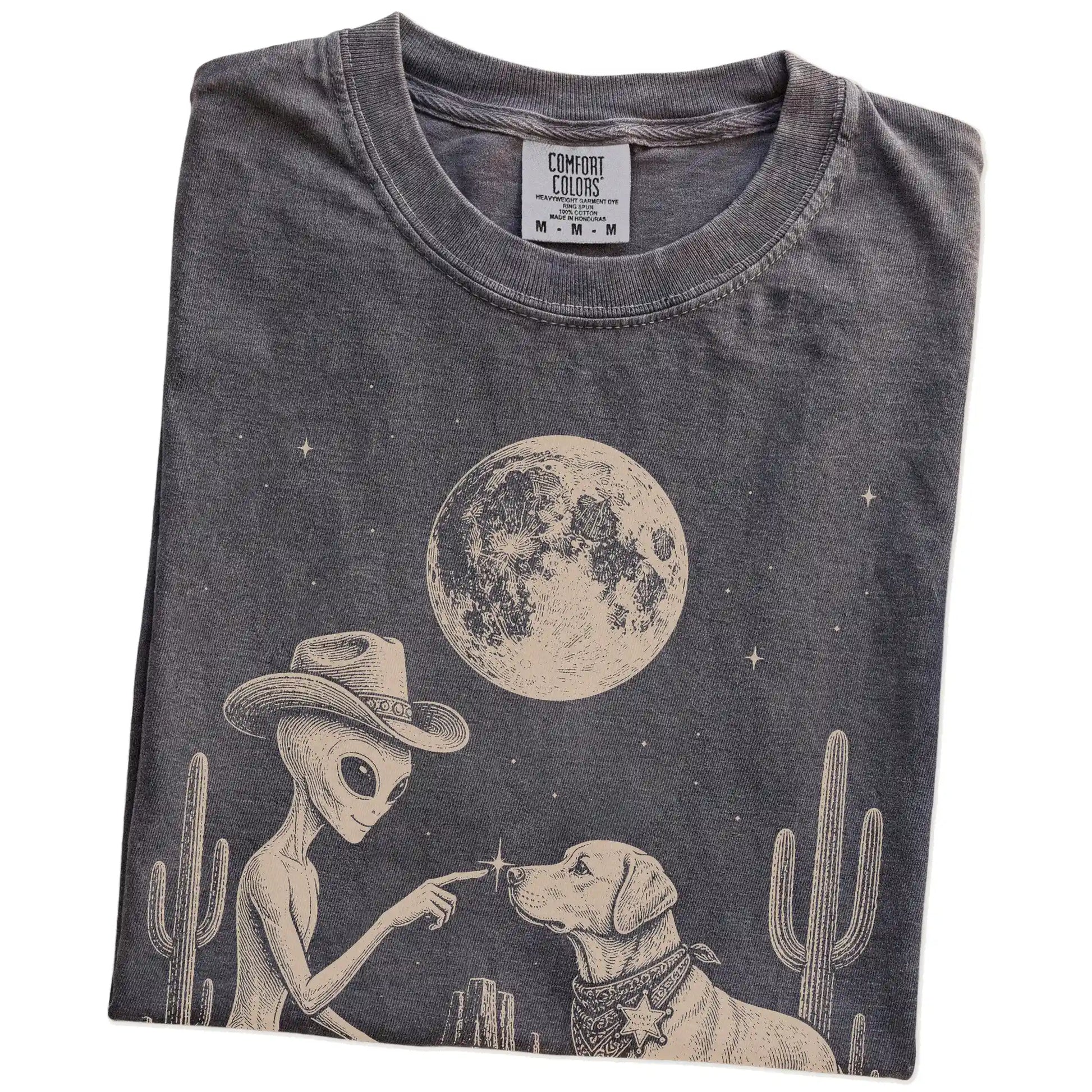 Folded Pepper Comfort Colors® T-shirt showing cowboy alien fist-bumping a labrador retriever beneath the moon