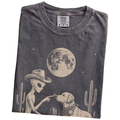 Folded Pepper Comfort Colors® T-shirt showing cowboy alien fist-bumping a labrador retriever beneath the moon