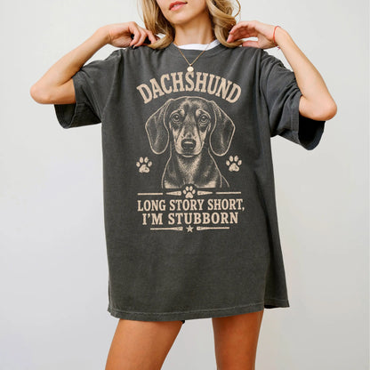Model wearing a Pepper Comfort Colors® T-shirt featuring Dachshund design with “Long Story Short, I'm Stubborn” lettering
