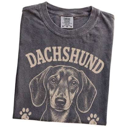 Folded Pepper Comfort Colors® T-shirt showing Dachshund design with “Long Story Short, I'm Stubborn” lettering