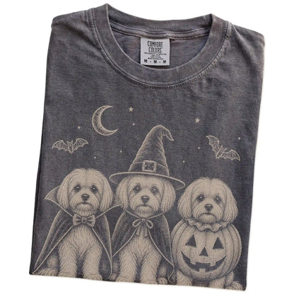 Folded Pepper Comfort Colors® T-shirt showing three Maltese dogs dressed for Halloween beneath bats and a crescent moon