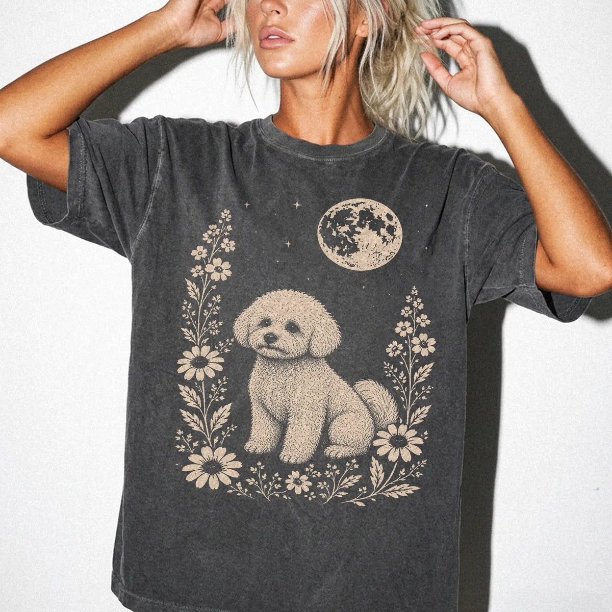 Model wearing a Pepper Comfort Colors® T-shirt featuring Bichon Frise framed by flowers beneath the moon