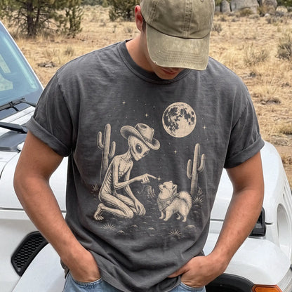 Model wearing a Pepper Comfort Colors® T-shirt with cowboy alien fist-bumping a pomeranian beneath the moon