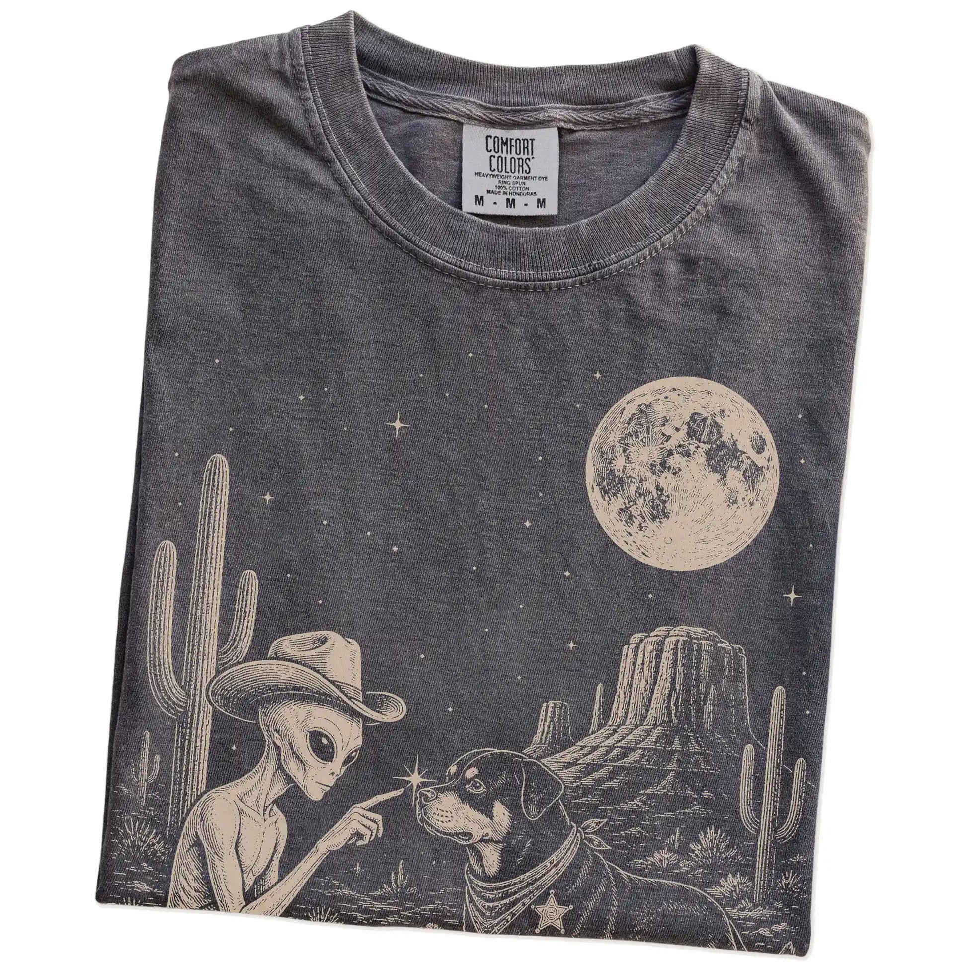 Folded Pepper Comfort Colors® T-shirt showing cowboy alien fist-bumping a rottweiler beneath the moon