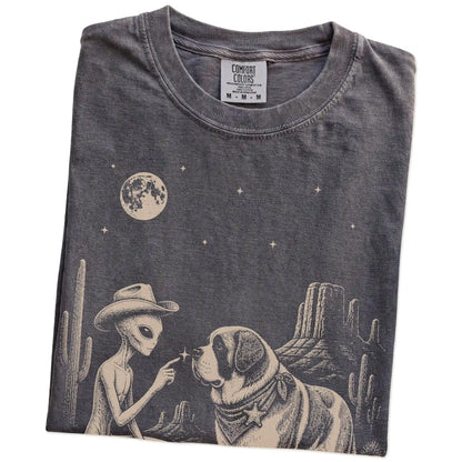 Folded Pepper Comfort Colors® T-shirt showing cowboy alien fist-bumping a saint bernard beneath the moon