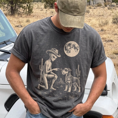 Model wearing a Pepper Comfort Colors® T-shirt with cowboy alien fist-bumping a schnauzer beneath the moon
