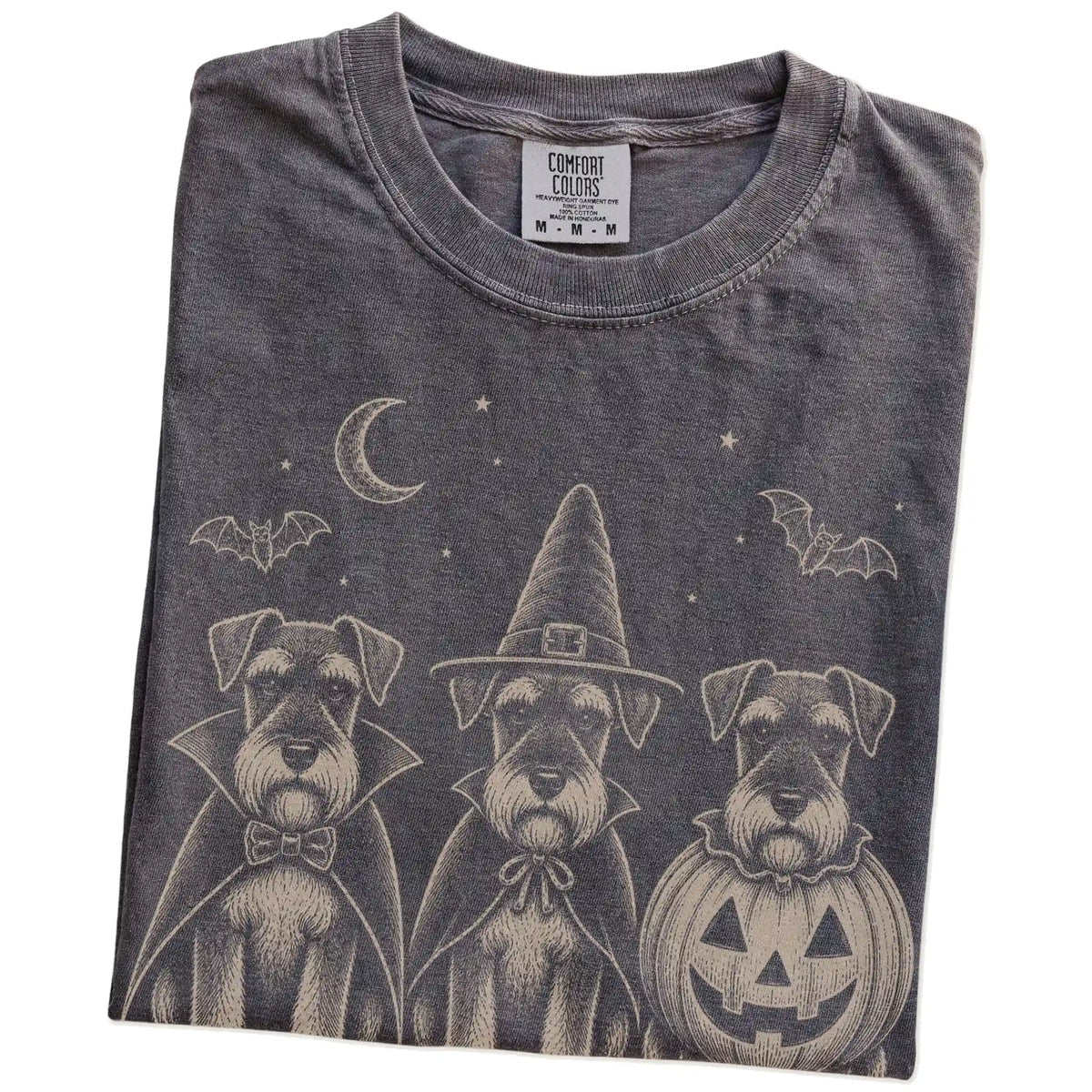 Folded Pepper Comfort Colors® T-shirt showing three Schnauzer dogs dressed for Halloween beneath bats and a crescent moon