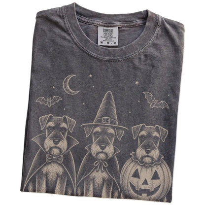Folded Pepper Comfort Colors® T-shirt showing three Schnauzer dogs dressed for Halloween beneath bats and a crescent moon