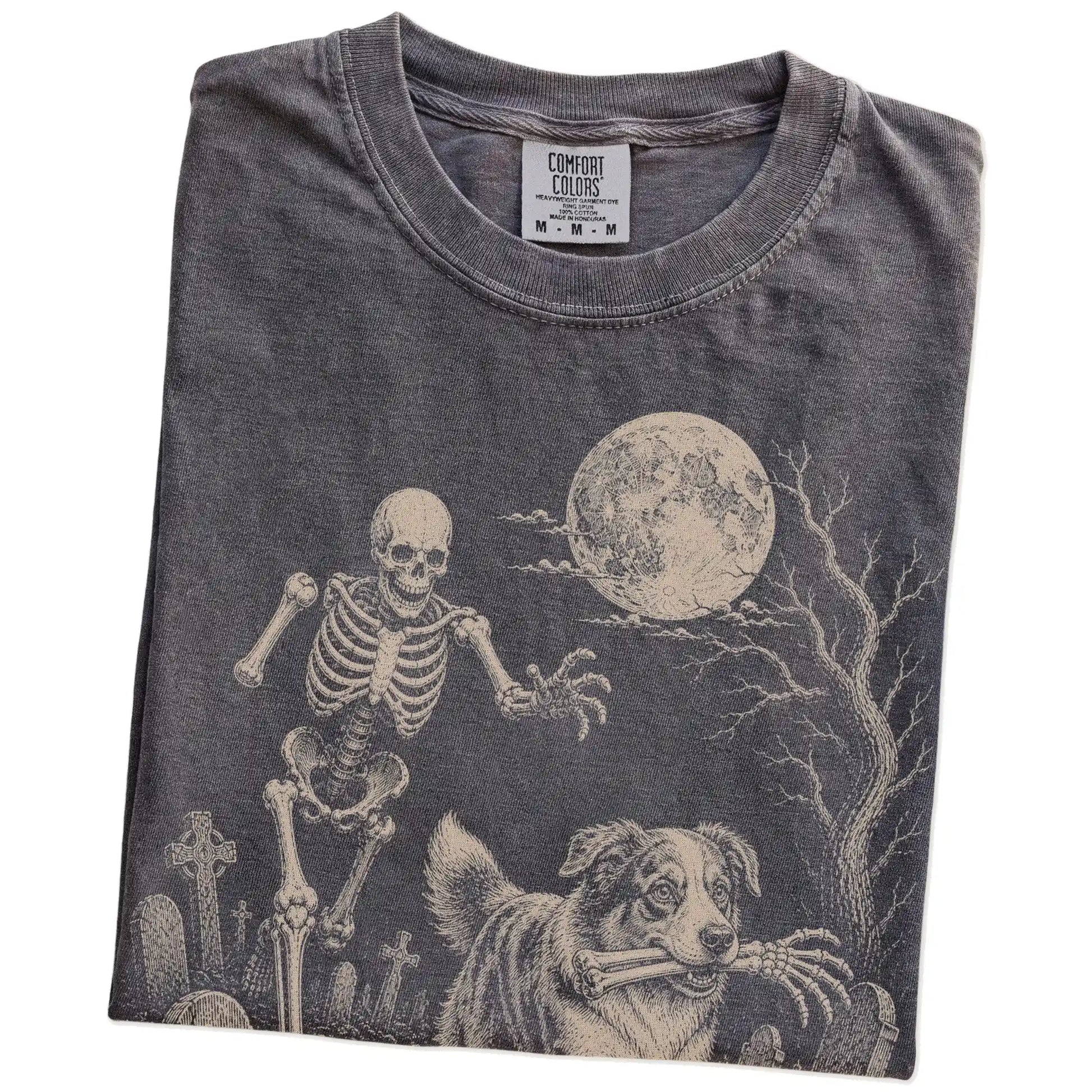 Folded Pepper Comfort Colors® T-shirt showing Australian Shepherd running through a moonlit graveyard with a chasing skeleton