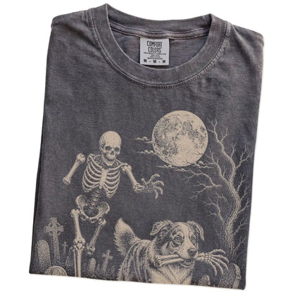 Folded Pepper Comfort Colors® T-shirt showing Australian Shepherd running through a moonlit graveyard with a chasing skeleton