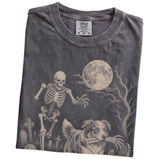 Folded Pepper Comfort Colors® T-shirt showing Australian Shepherd running through a moonlit graveyard with a chasing skeleton