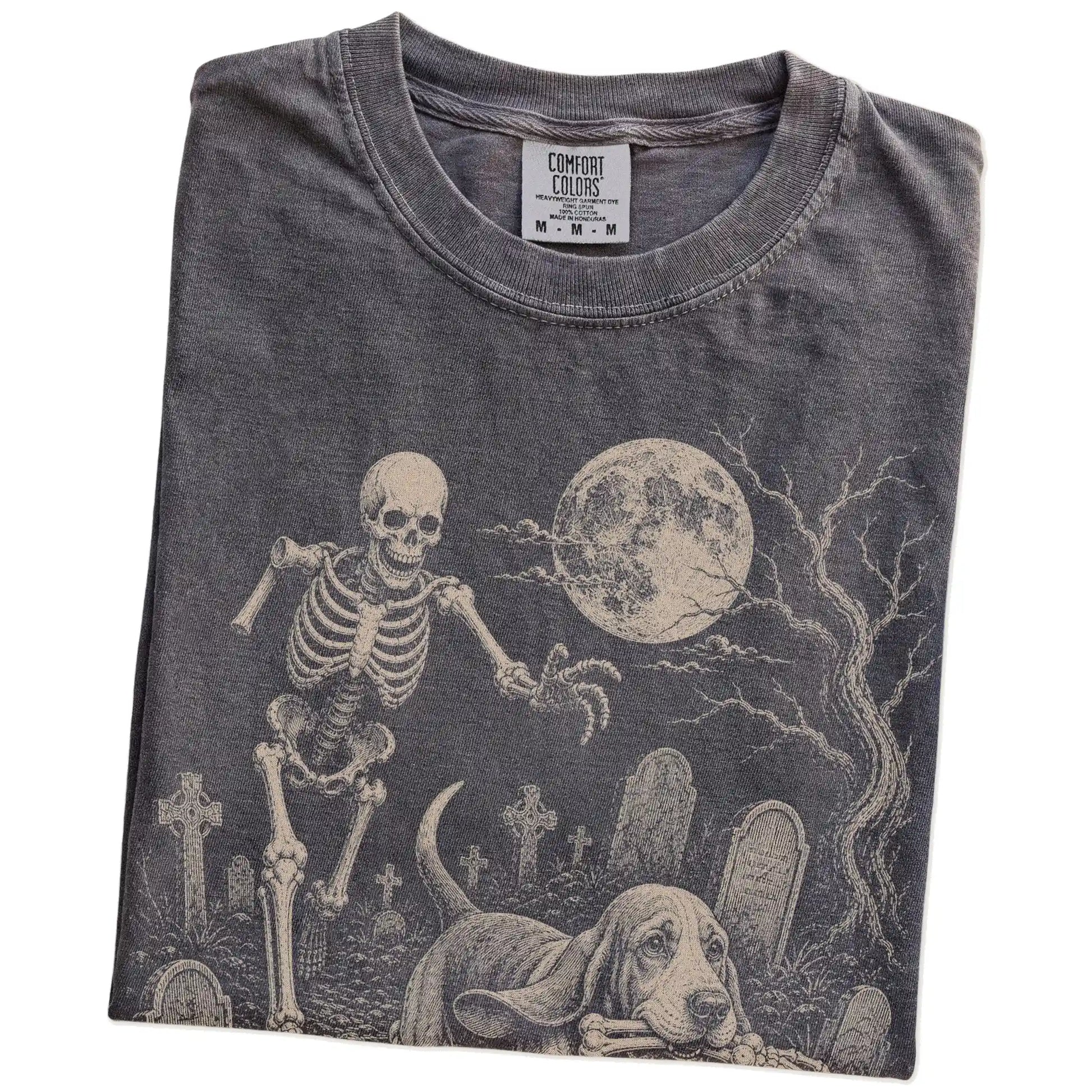 Folded Pepper Comfort Colors® T-shirt showing Basset Hound running through a moonlit graveyard with a chasing skeleton