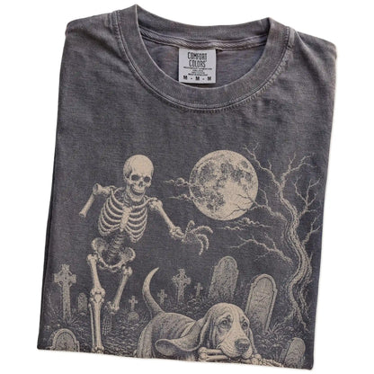Folded Pepper Comfort Colors® T-shirt showing Basset Hound running through a moonlit graveyard with a chasing skeleton