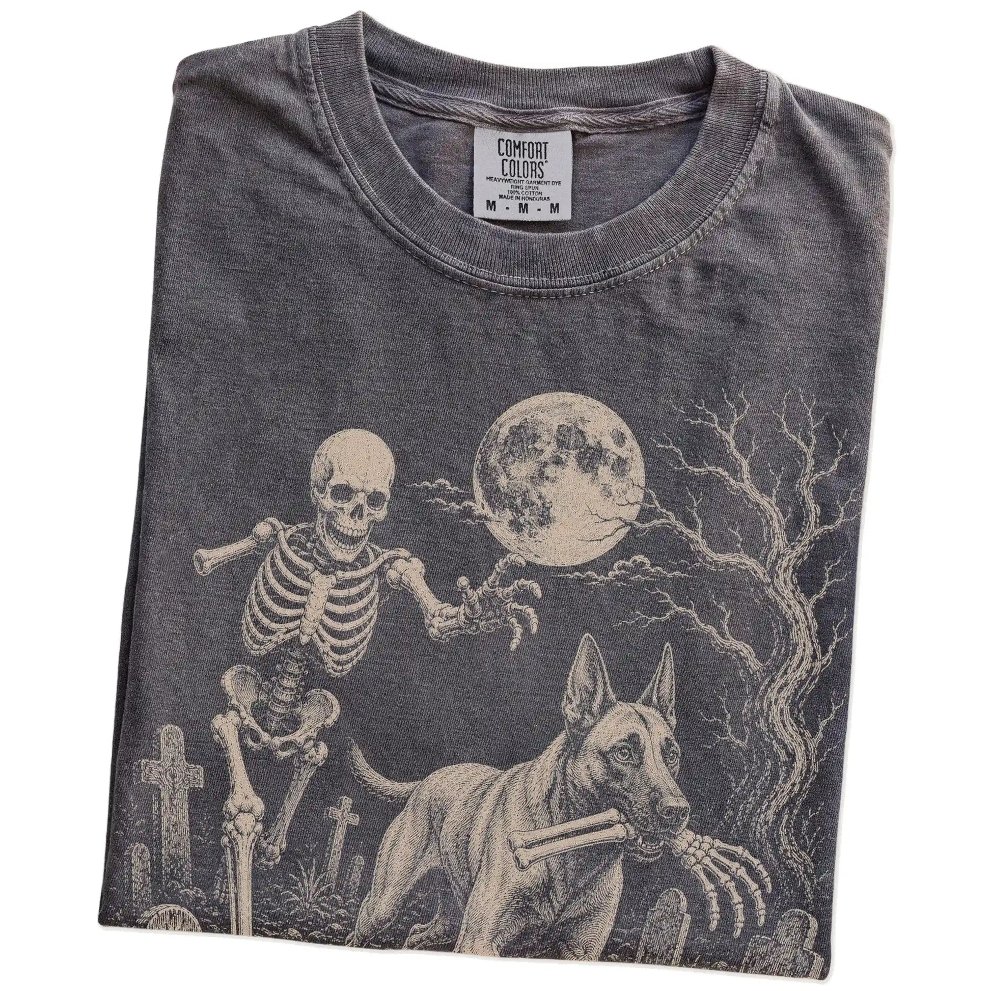 Folded Pepper Comfort Colors® T-shirt showing Belgian Malinois running through a moonlit graveyard with a chasing skeleton