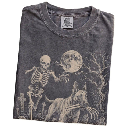 Folded Pepper Comfort Colors® T-shirt showing Belgian Malinois running through a moonlit graveyard with a chasing skeleton