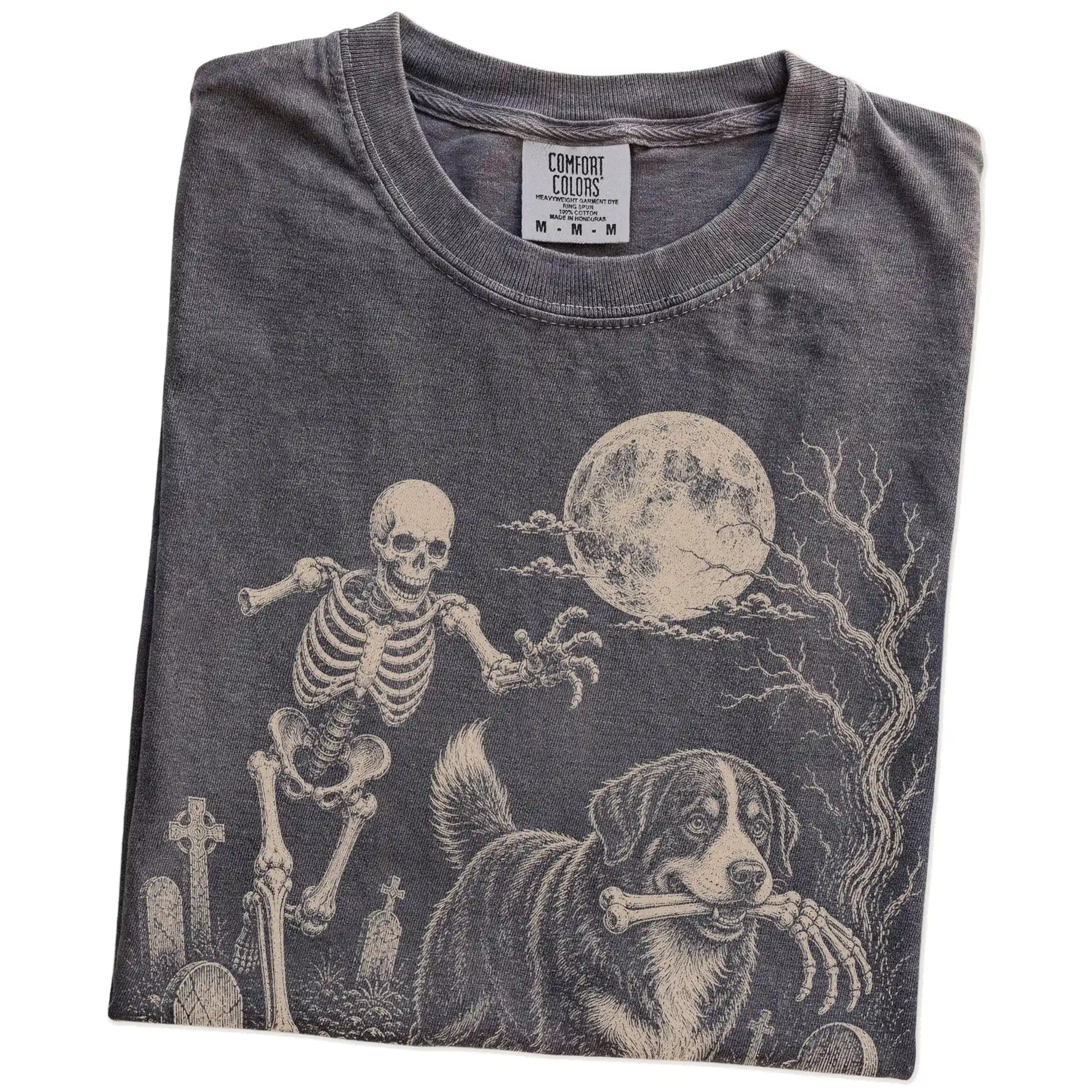 Folded Pepper Comfort Colors® T-shirt showing Bernese Mountain Dog running through a moonlit graveyard with a chasing skeleto